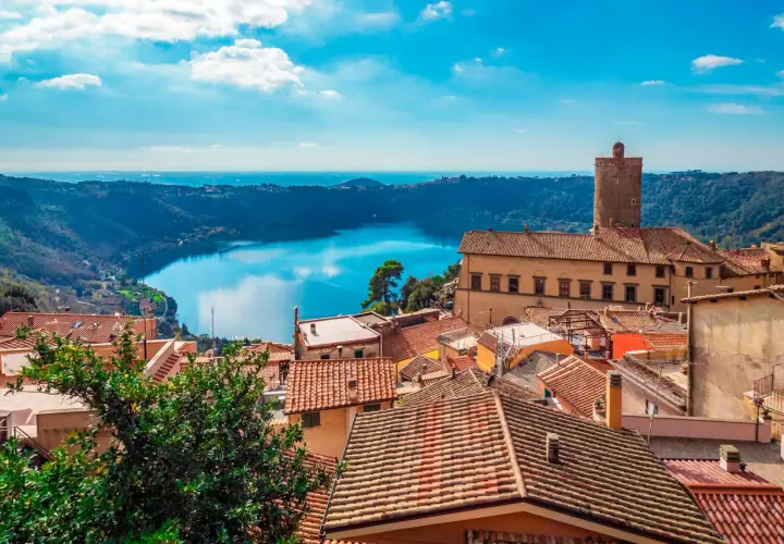 Panoramica dei Castelli Romani in moto: tetti rossi, un lago blu e un cielo terso.