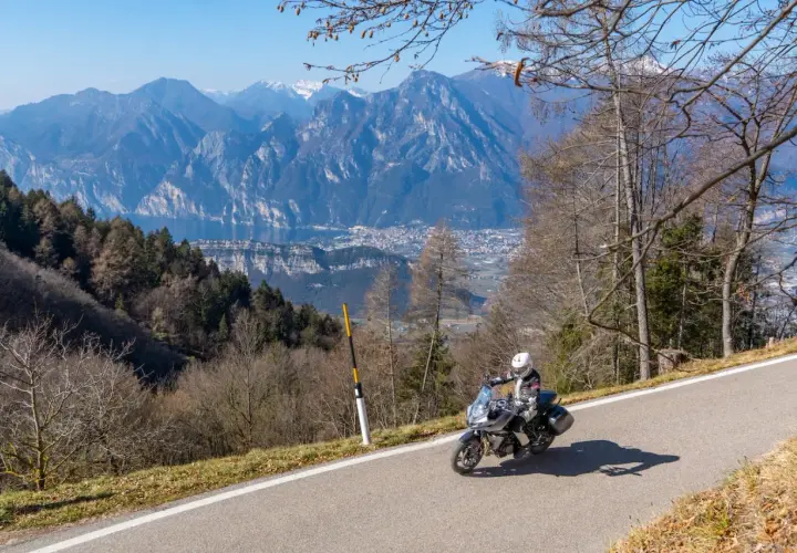 Un motociclista si gode un giro in moto sul Lago di Garda, con montagne maestose e un villaggio sullo sfondo.