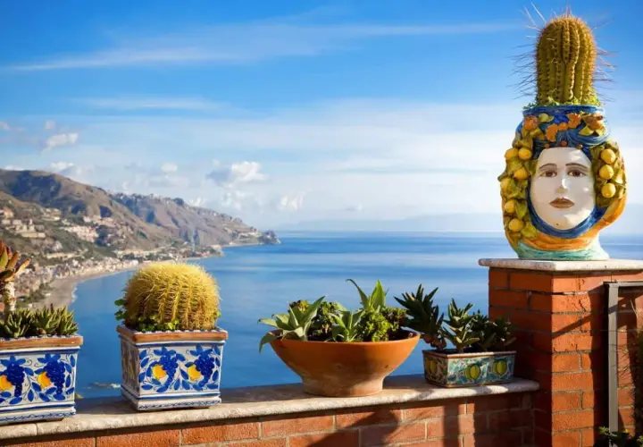 Balcone fiorito con vista sul mare, tra i posti più belli della Sicilia. Cactus e vasi decorati con teste di moro.