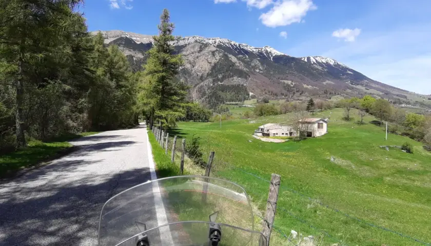 Strada di montagna, un'avventura in moto verso la punta veleno. Paesaggio verdeggiante, montagne innevate e cielo azzurro.