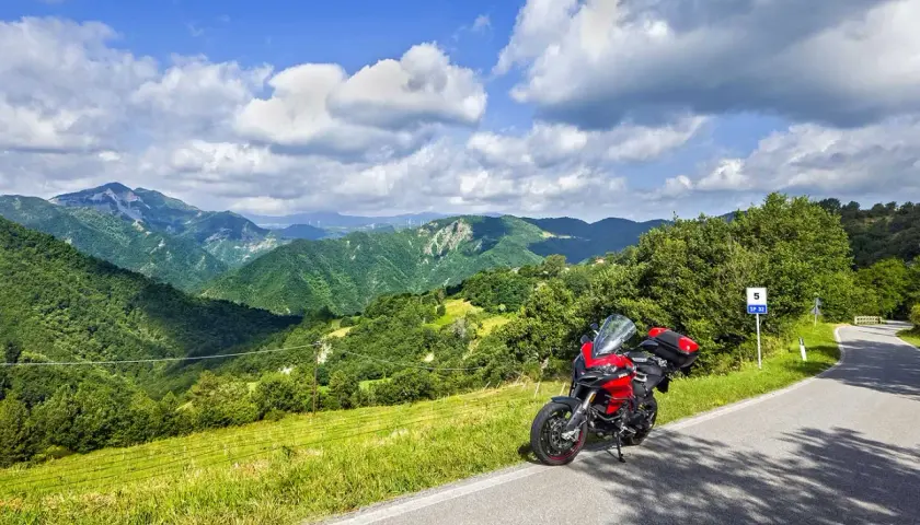 Ducati rossa ferma sul ciglio della strada statale 67, con un panorama mozzafiato di colline verdi e cielo azzurro.