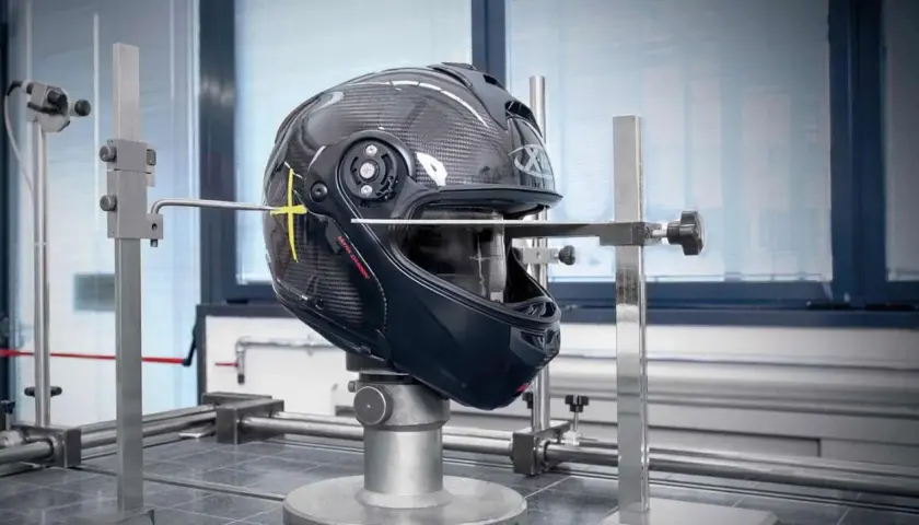 Casco da moto in carbonio sottoposto a test per l'omologazione, con strumenti di misurazione che ne verificano la resistenza e la sicurezza.