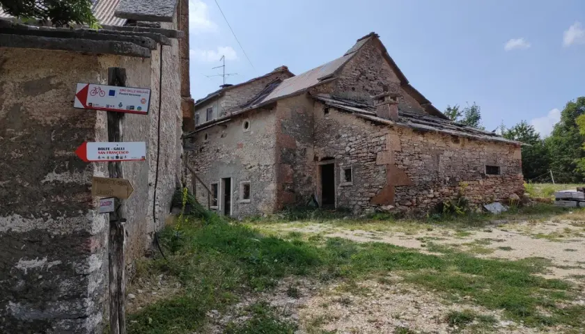 Un vecchio parparo in pietra, con tetto in lamiera e tegole, mostra cartelli per sentieri escursionistici e ciclabili.