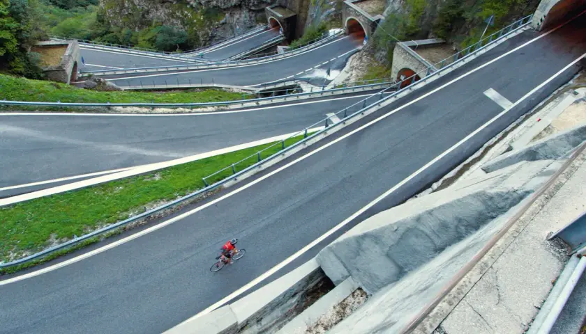 Ciclista solitario affronta i tornanti del passo Bidibidì, tra gallerie scavate nella roccia e panorami mozzafiato.