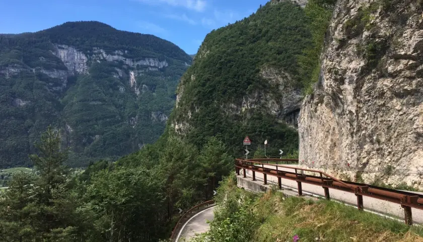 Strada panoramica sul Passo Manghen, con montagne verdi e un cielo azzurro.