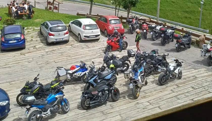 Un gruppo di motociclisti si ferma per una pausa al passo Zambla, con moto parcheggiate accanto ad alcune auto.