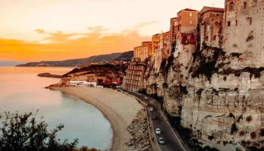 Tramonto mozzafiato sulla costa, con case aggrappate alla scogliera. Un sogno di **Calabria in moto**.