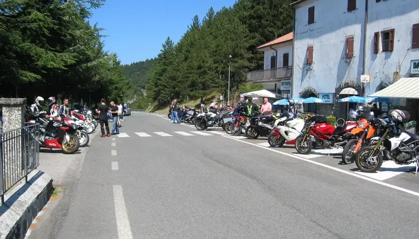Gruppo di motociclisti in sosta lungo la strada statale 67 Tosco Romagnola, con moto parcheggiate e un hotel sullo sfondo.