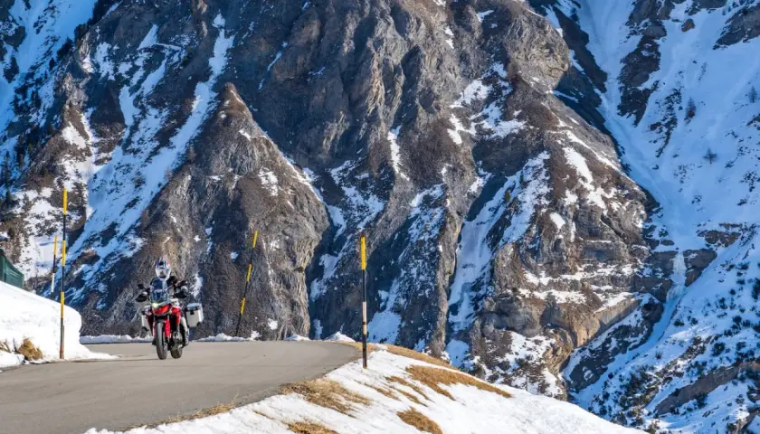 Motociclista su strada innevata tra le montagne, un viaggio da Bolzano a Livigno.