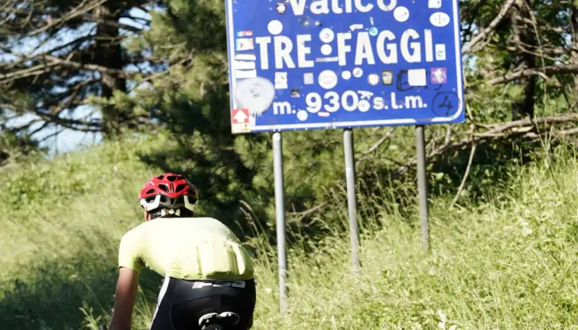 Ciclista in cima al valico Tre Faggi, 930 metri sul livello del mare, tra alberi e erba alta.
