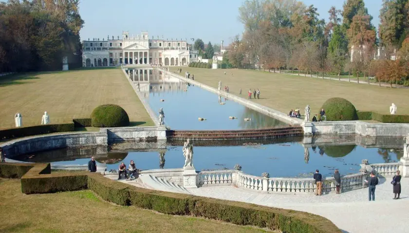 Un'imponente villa con un lungo specchio d'acqua e giardini curati, che ricorda le ville palladiane.