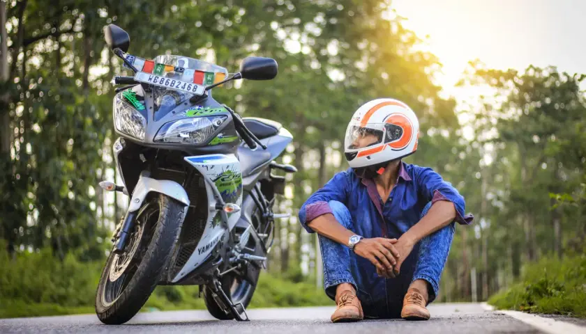 Giovane con casco arancione e bianco, seduto accanto alla sua moto. Spera di allargare il casco stretto per un viaggio più comodo.