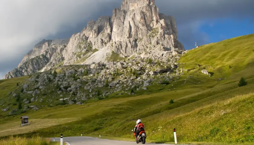 Motociclista in viaggio verso il passo del cerro, con imponenti montagne sullo sfondo e verdi pendii erbosi.