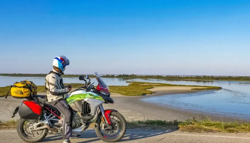 Motociclista con moto da turismo si ferma lungo la strada statale 9 Via Emilia, con una laguna sullo sfondo.