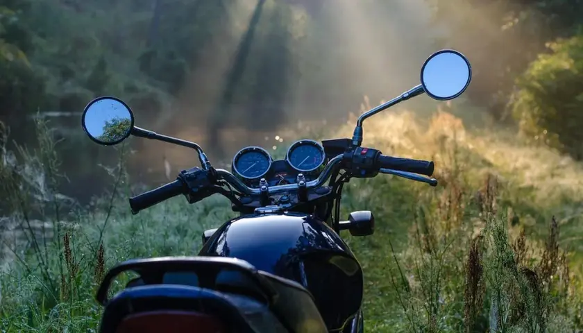Manubrio di moto scura in un prato nebbioso, pronto per esplorare i borghi lombardia in moto all'alba.