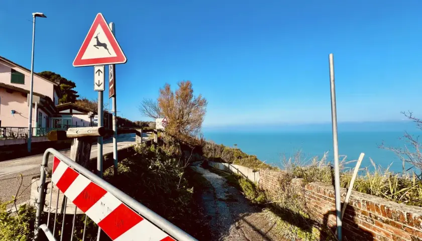 Panoramica Gabicce con segnale di pericolo cervi e mare azzurro. Strada sterrata con muretto in mattoni.