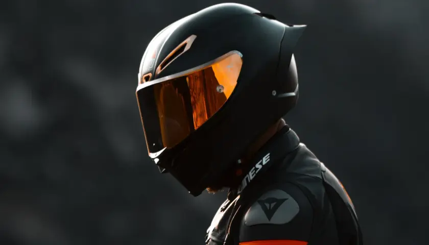 Un motociclista indossa un casco integrale nero con visiera arancione riflettente, pronto per la pista.