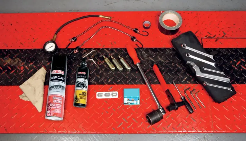Kit di attrezzi da portare in moto: grasso catena, pulitore, chiavi, brugole, compressore portatile e nastro adesivo.