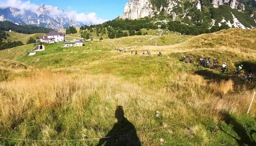 Gruppo di ciclisti in discesa su un sentiero erboso, con montagne imponenti sullo sfondo. Un'avventura a Recoaro 1000.