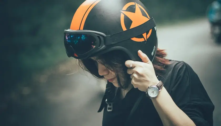 Ragazza con casco da moto nero e arancione, occhiali riflettenti. Dove mettere il casco della moto? Forse qui, prima di partire.
