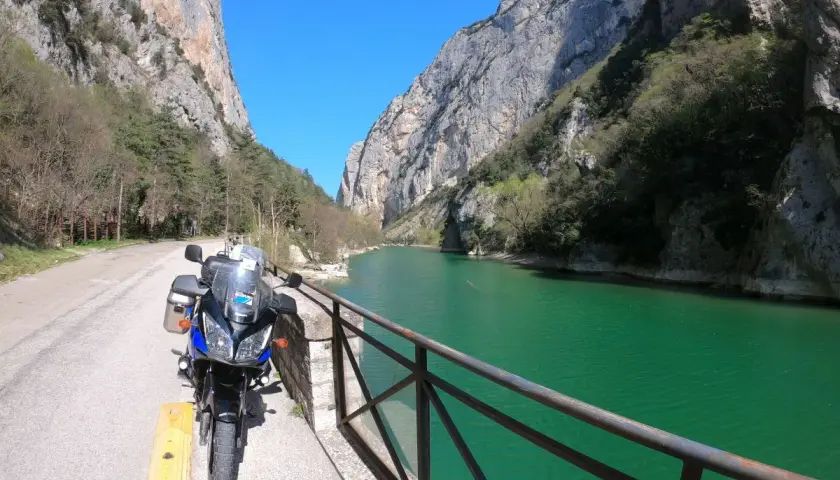 Moto parcheggiata lungo la strada panoramica delle Gole del Furlo, con il fiume color smeraldo e le imponenti pareti rocciose.