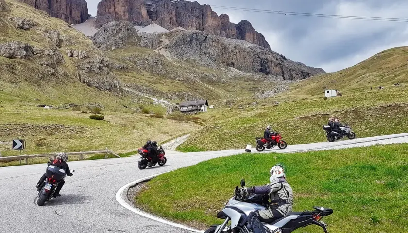 Motociclisti in gruppo affrontano le curve del passo della Cappelletta, tra verdi pendii e imponenti pareti rocciose.