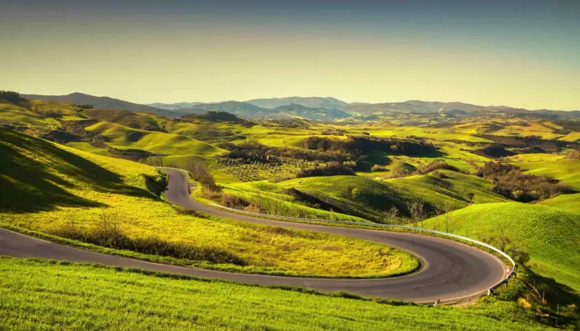 Strada volterrana serpeggiante tra dolci colline verdi sotto un cielo limpido.