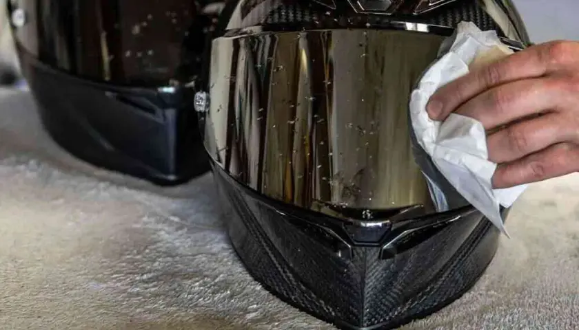 Mano che pulisce la visiera del casco con un panno bianco, rimuovendo insetti e sporco per una guida sicura.