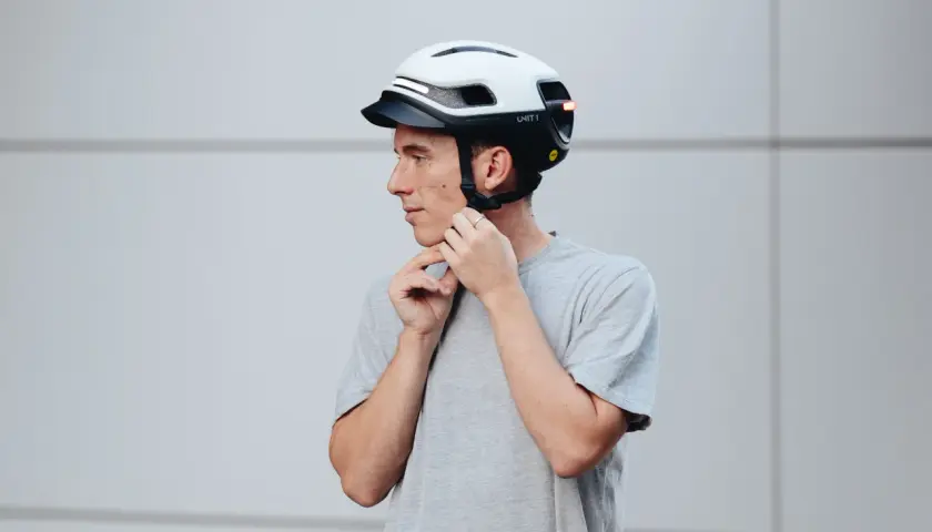 Uomo con casco bianco e nero, che regola gli spallacci. Le taglie caschi sono fondamentali per la sicurezza.