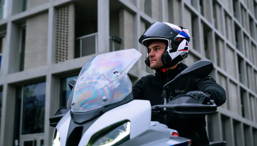 Motociclista con casco modulare, che può essere jet o integrale, pronto a partire con la sua moto davanti a un edificio moderno.
