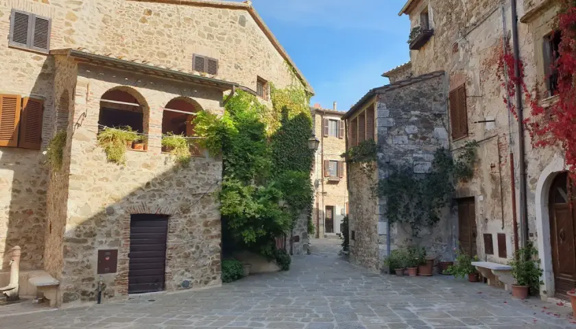 Un vicolo pittoresco a Montemerano, con case in pietra, archi, piante rampicanti e un cielo azzurro. Scopri cosa vedere in questo borgo incantevole.