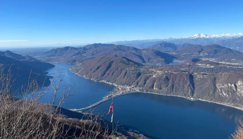 Vista mozzafiato dal balcone d'Italia. Un lago blu intenso abbraccia montagne boscose, con un ponte che attraversa le acque. Perfetto per un viaggio in moto.