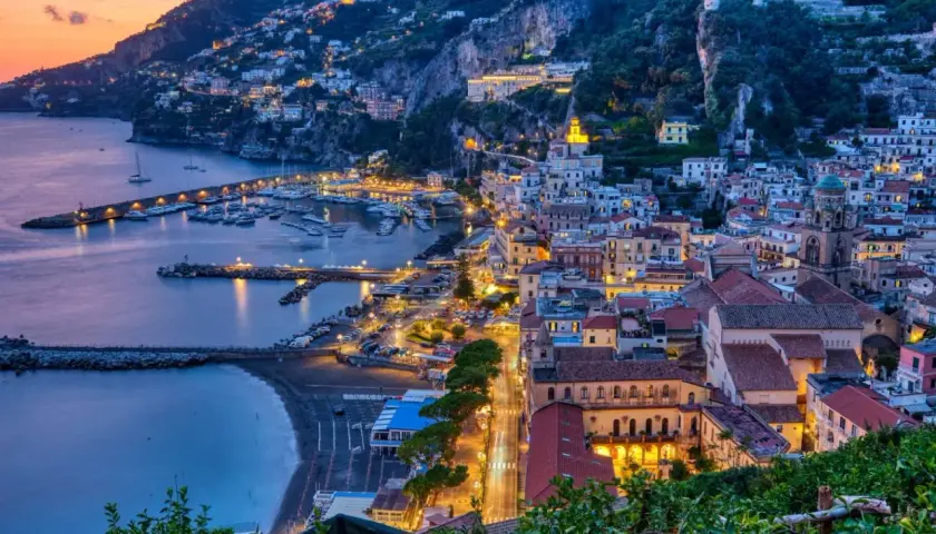Le luci illuminano le case aggrappate alla costa e il porto turistico. Le strade costiera amalfitana prendono vita al tramonto.