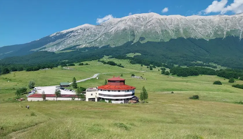 Edificio circolare con tetto rosso e montagne sullo sfondo, al passo San Leonardo.