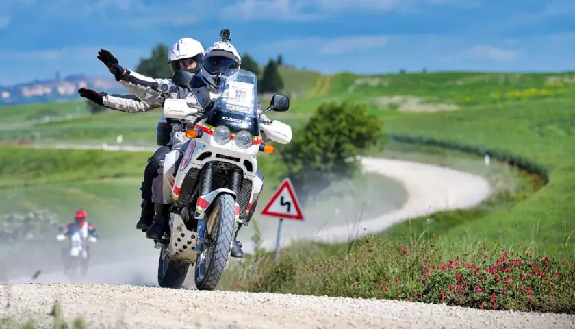 Coppia in moto su sterrato, seguendo una mappa percorso eroica in moto tra colline verdi.