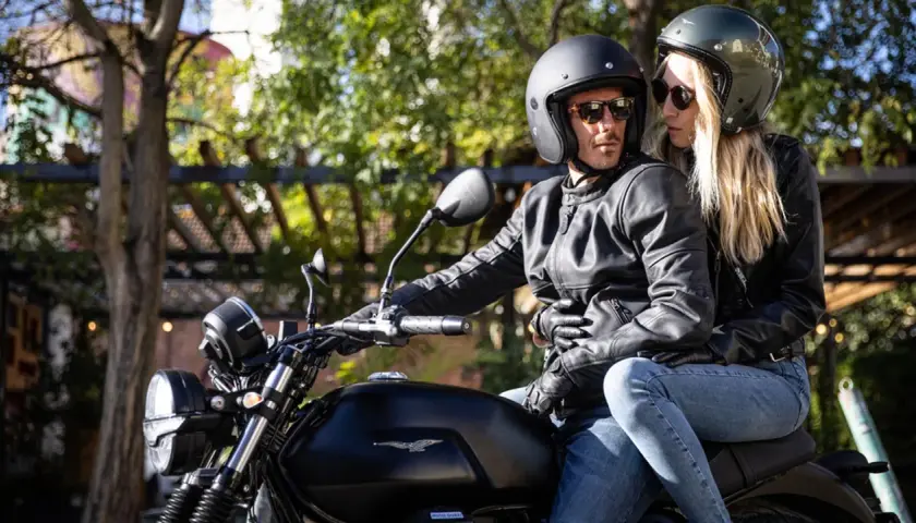 Coppia in moto, lei mostra come vestirsi per andare in moto donna con giacca in pelle e jeans.