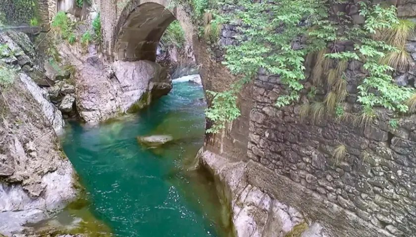 Acqua smeraldo scorre sotto un antico ponte di pietra, creando un'atmosfera suggestiva nell'orrido Val Taleggio.