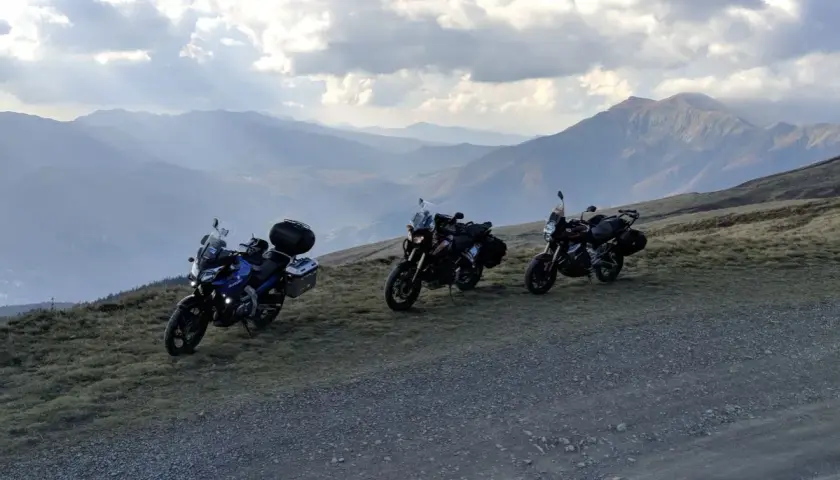 Tre moto attendono al Passo dell'Abetone, con un panorama montano mozzafiato sotto un cielo nuvoloso.