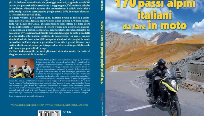Motociclista in cima a un passo alpino, con montagne sullo sfondo. Un invito a scoprire 170 passi alpini italiani da fare in moto.
