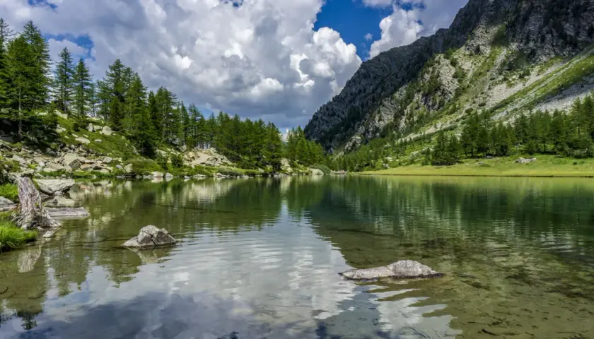 Un lago alpino tranquillo riflette il cielo nuvoloso e le montagne boscose. Un paesaggio mozzafiato dei laghi della Valle d'Aosta.