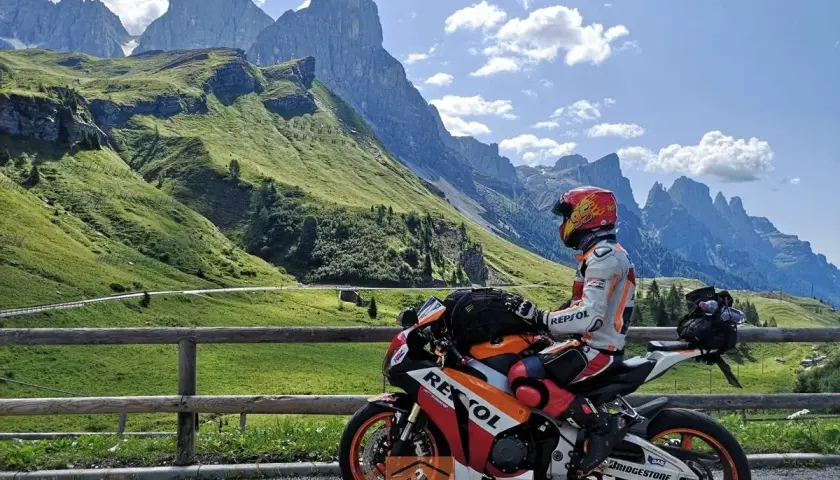 Motociclista in tenuta da gara su una Honda Repsol, con lo sfondo delle maestose vette del Passo Cereda.