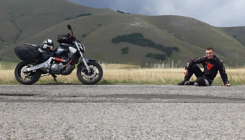 Motociclista in tenuta da gara seduto sul ciglio della strada al passo San Antonio, con la sua moto parcheggiata accanto.