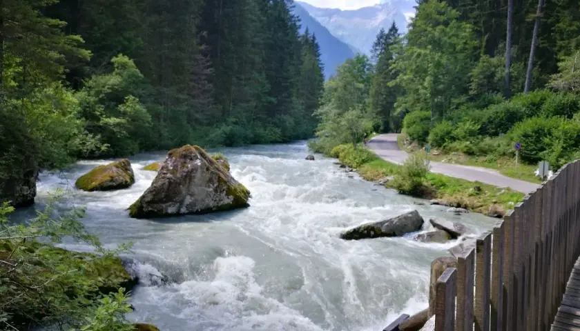 Fiume impetuoso tra rocce e boschi, con una strada serpeggiante e montagne sullo sfondo, ricorda le cascate del Nardis.