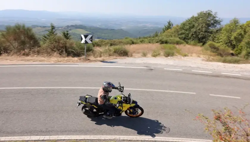 Motociclista in viaggio da Firenze a Siena, attraversa una strada panoramica tra le colline toscane sotto un cielo azzurro.