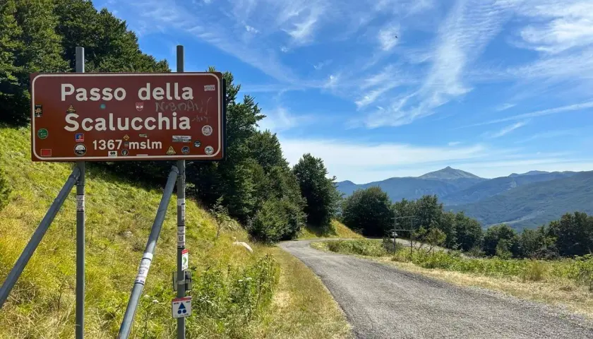 Cartello stradale indica Passo della Scalucchia a 1367 metri. La strada sale tra alberi e montagne sullo sfondo.