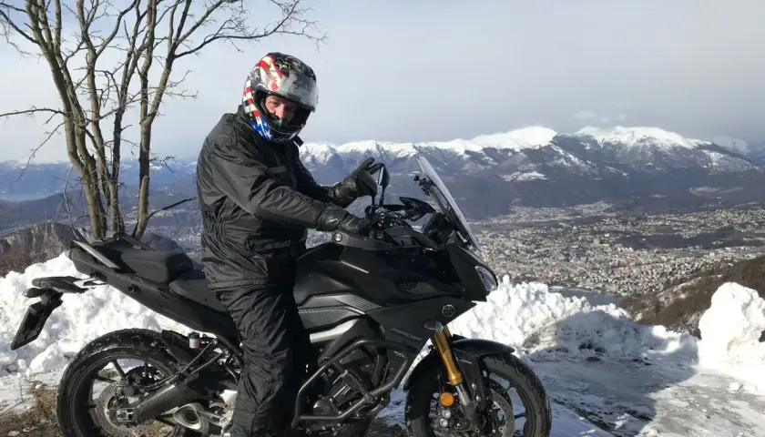 Motociclista con casco stellato su un balcone d'Italia innevato, con vista su montagne e città.