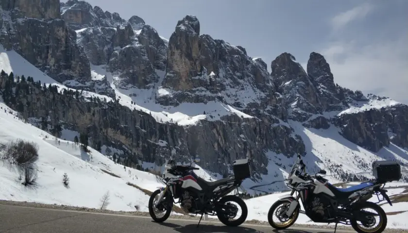 Due moto da enduro parcheggiate su una strada innevata, con imponenti vette delle valli bergamasche sullo sfondo.