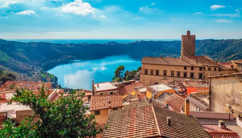 Panoramica dei Castelli Romani in moto: tetti rossi, un lago blu e un cielo terso.