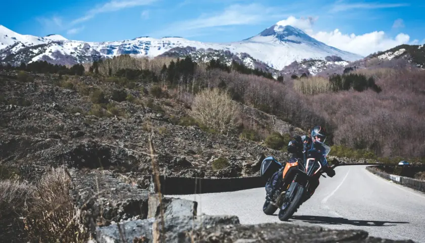 Motociclista su strada mareneve, con vulcano innevato sullo sfondo.
