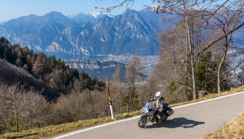 Un motociclista si gode un giro in moto sul Lago di Garda, con montagne maestose e un villaggio sullo sfondo.